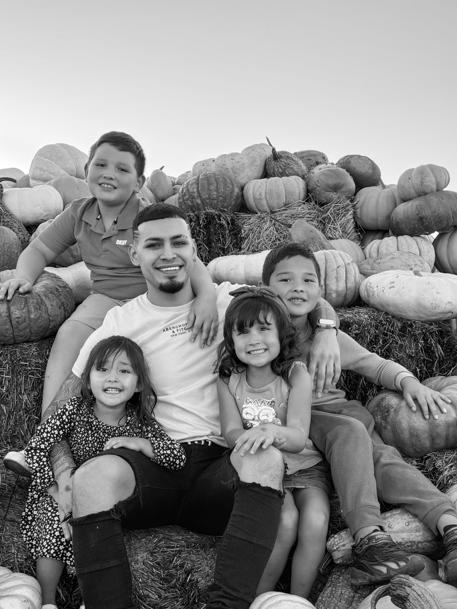 A group of children gathered among hay bales and pumpkins at the farm